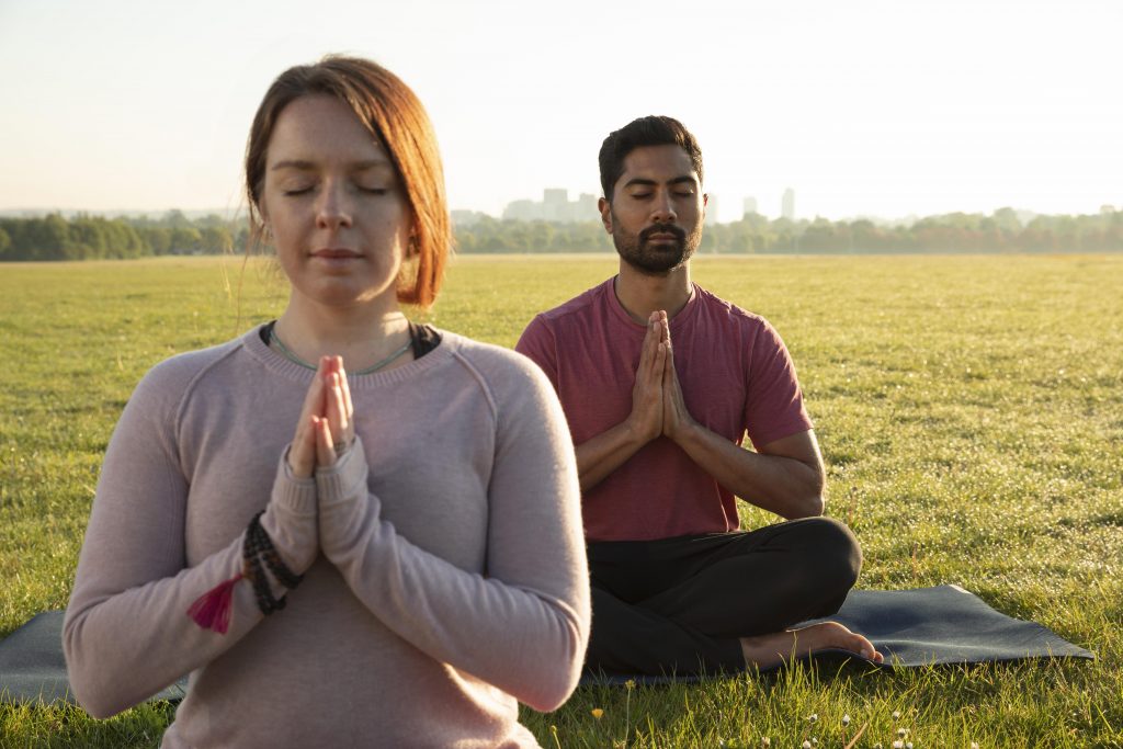 Two people meditating side by side, one with a focused expression and the other with a relaxed expression, representing the different 